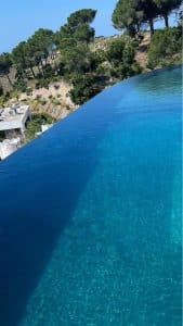Piscine à débordement minimaliste avec effet miroir, surplombant un paysage naturel méditerranéen.
