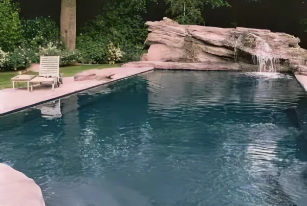 Piscine paysagée en béton avec rochers décoratifs et cascade intégrée, entourée de végétation dense