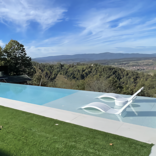Vue sur une piscine à débordement avec plage immergée et transat, face à un paysage vallonné