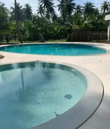 Piscine miroir à débordement en forme libre avec pataugeoire circulaire au premier plan, intégrée dans une terrasse continue