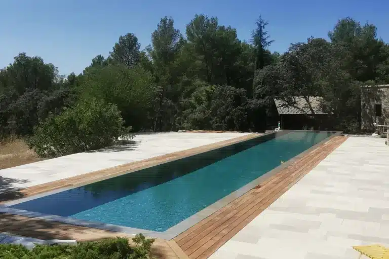 Vue générale du couloir de nage à débordement miroir de 25 m en Provence, avec plage immergée et terrasse en pierre et bois.