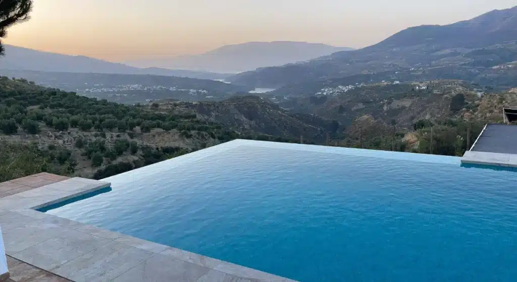Piscine à débordement intégrée à un terrain en pente, exemple d’architecture de piscine en continuité avec le paysage naturel.