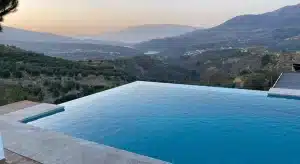 Piscine à débordement intégrée à un terrain en pente, exemple d’architecture de piscine en continuité avec le paysage naturel.